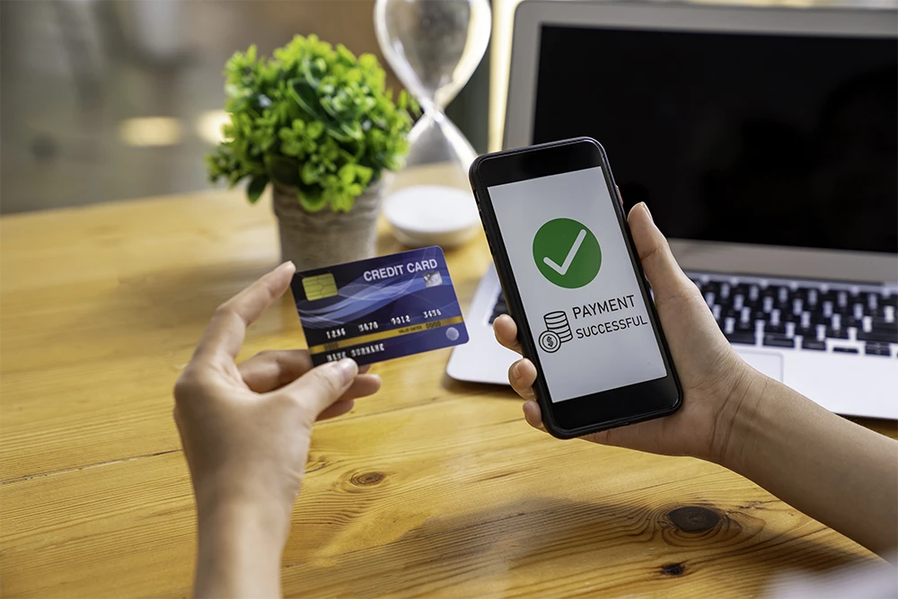 Hand holding a smartphone to review business payment details with a laptop in the background